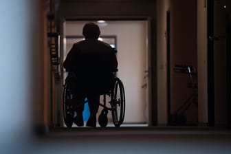 Eine Frau sitzt in einem Heim in einem Rollstuhl auf einem Gang