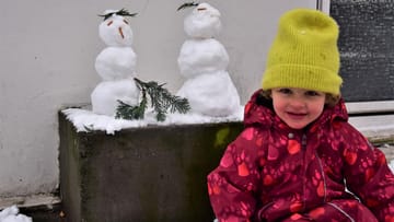 Ein Kind sitzt neben ihren Schneemännern: Marie (4) aus Ottensen hatte Freude am Neuschnee in Hamburg.
