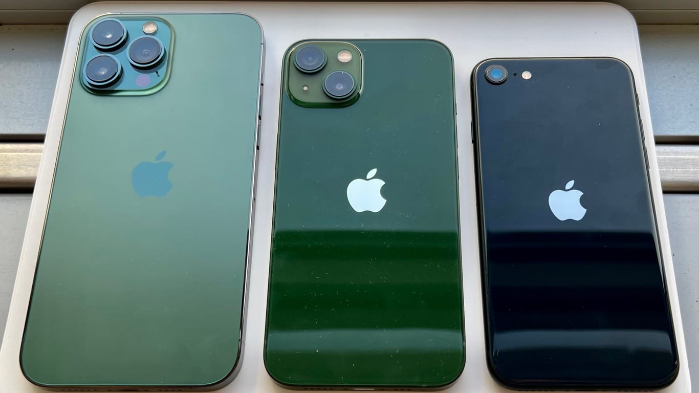 iPhone 13 Pro Max, iPhone 13 und iPhone SE (2022) von hinten. Das iPhone 13 Pro Max im neuen Alpin Grün, und das iPhone 13 im neuen Grün, das iPhone SE im altbekannten Schwarz.