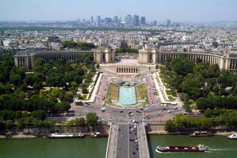 Blick vom Eiffelturm auf die französische Metropole mit der Seine und die Anlage Champs de Mars, am Horizont das Hochhaus-Viertel La Defense.