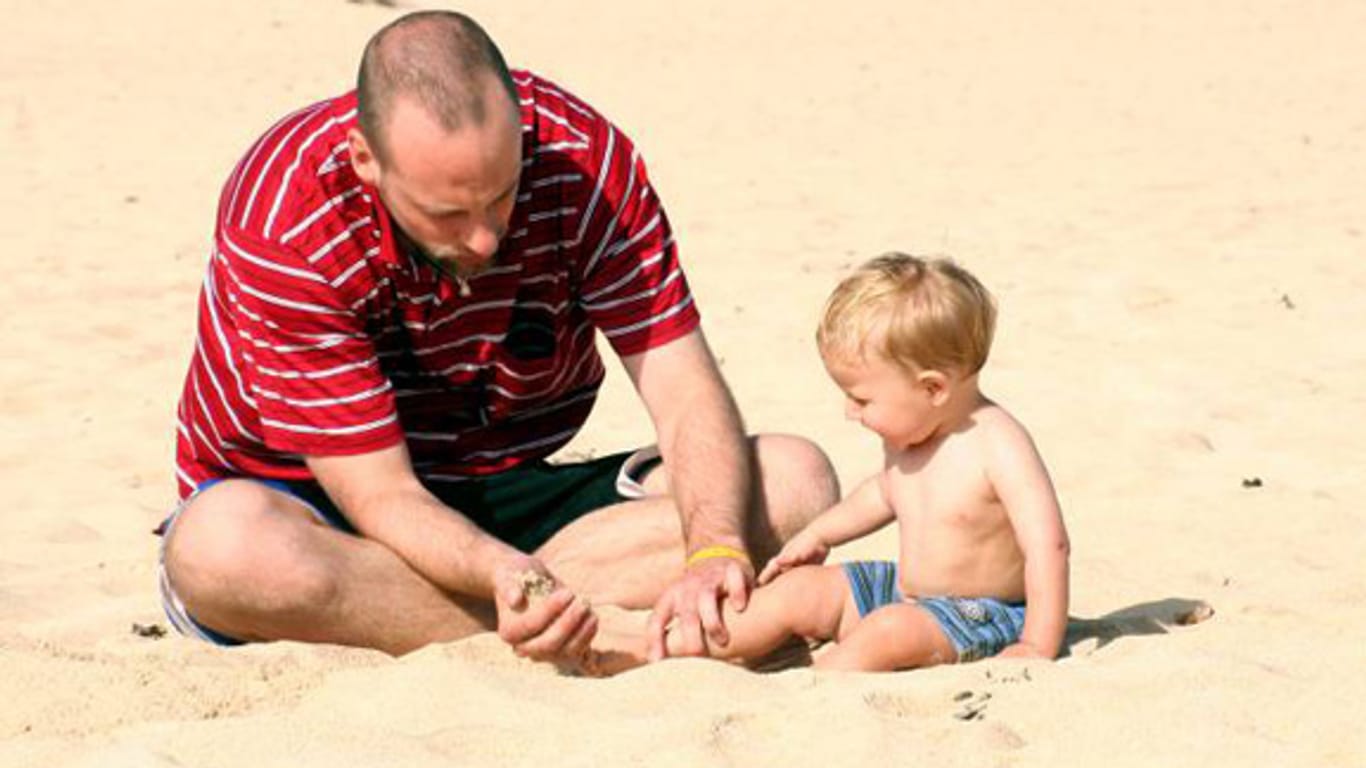 Vater spielt mit Kind am Strand.