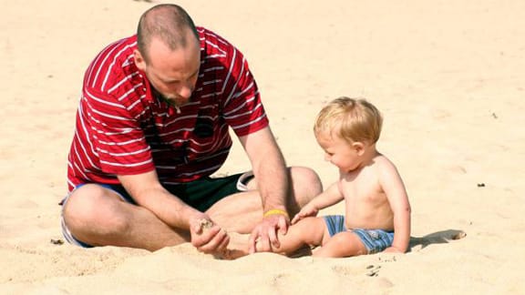 Vater spielt mit Kind am Strand.