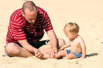 Vater spielt mit Kind am Strand.