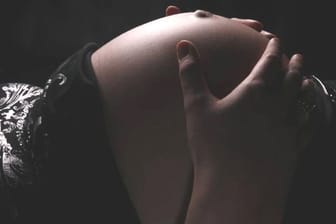 Schwangere hält die Hände an ihren Bauch.