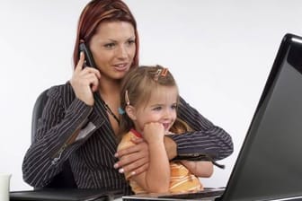 Junge Frau arbeitet am Computer, mit Kind auf dem Schoß.