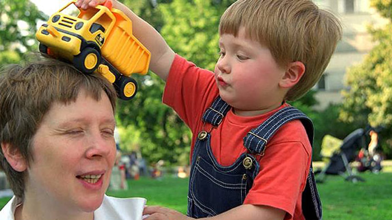 Kleiner Junge lässt sein Spielzeug-Auto über den Kopf seiner Mutter rollen.