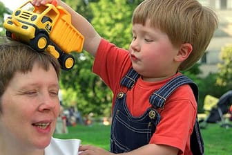 Kleiner Junge lässt sein Spielzeug-Auto über den Kopf seiner Mutter rollen.