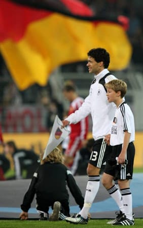 Michael Ballack im Trikot der Nationalmannschaft mit einem Jungen der Fußball-Eskorte.