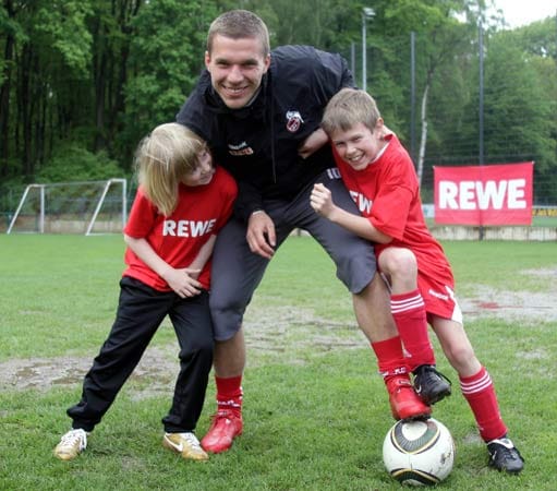Lukas Podolski mit zwei Kindern auf dem Fußballplatz.