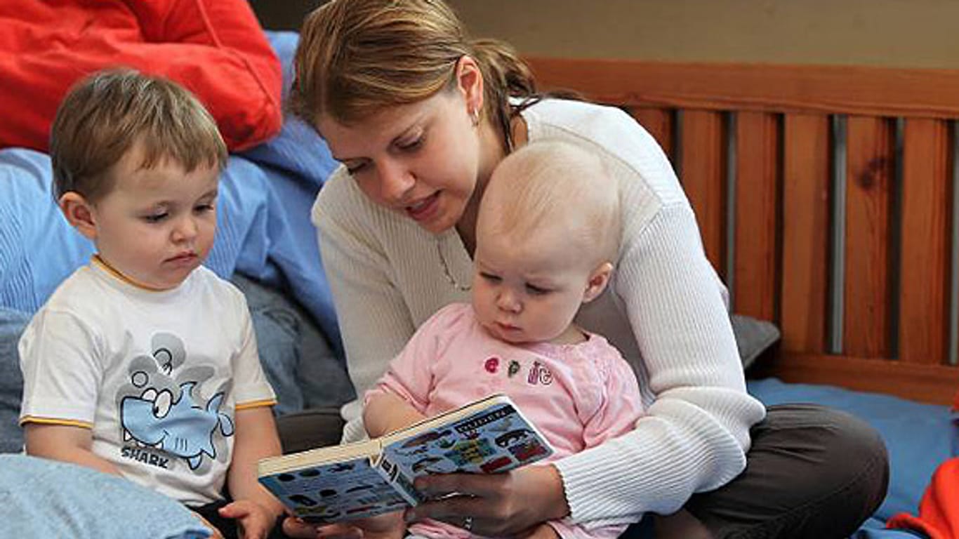 Betreuerin blättert mit zwei Kleinkindern in einem Kinderbuch.