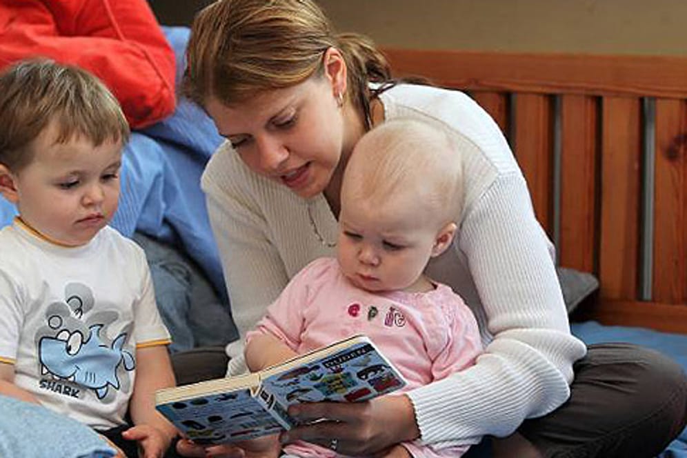 Betreuerin blättert mit zwei Kleinkindern in einem Kinderbuch.