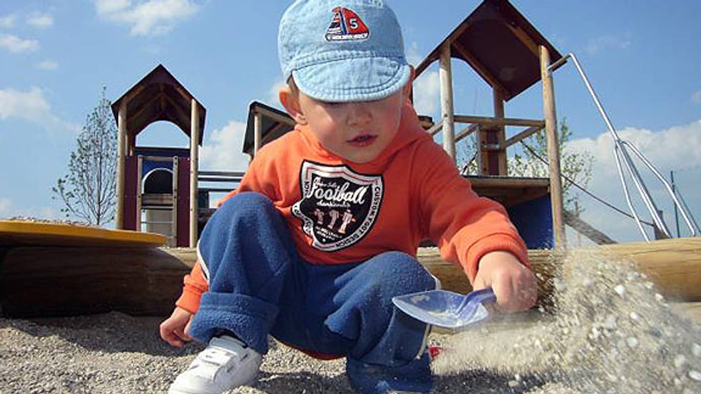 Kleiner Junge spielt mit seiner Schaufel im Sandkasten eines Spielplatzes.