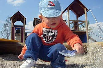 Kleiner Junge spielt mit seiner Schaufel im Sandkasten eines Spielplatzes.