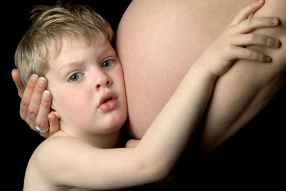 Ein kleiner junge umarmt den Bauch seiner schwangeren Mutter.