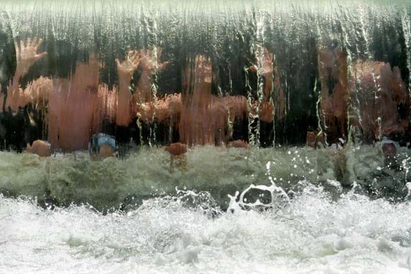 Jugendliche sitzen am Montag im Eisbach in München unter einem Wasserfall