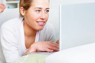 Jugendliches Mädchen liegt auf ihrem Bett und arbeitet am Laptop.
