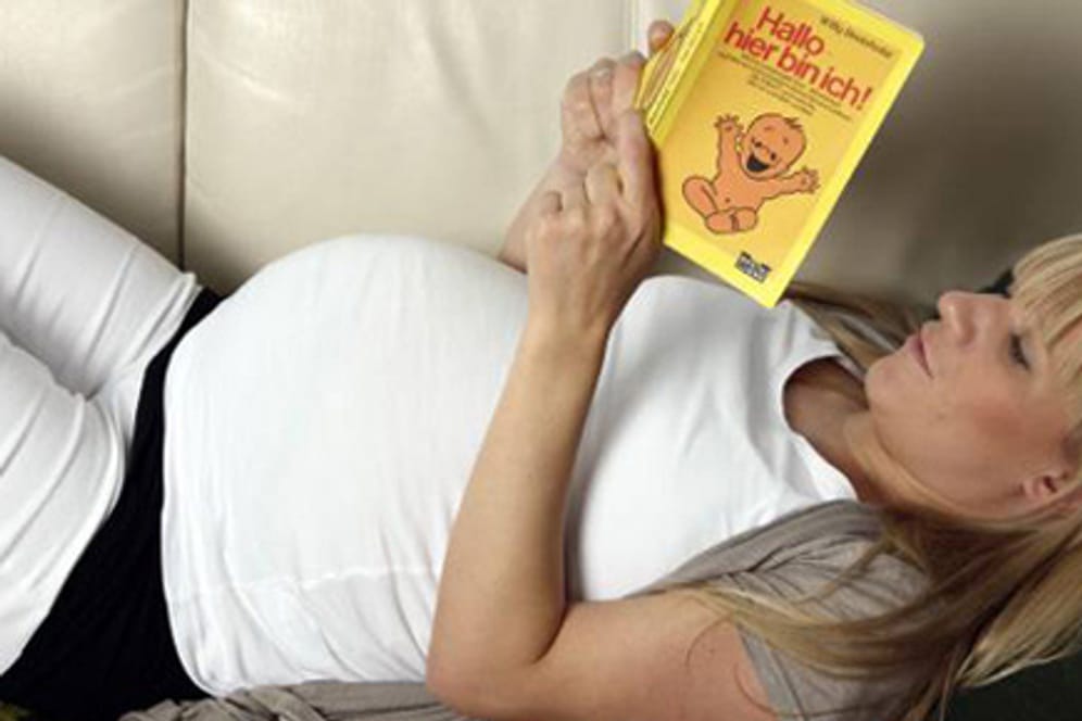 Schwangere im neunten Monat liest Ratgeber auf der Couch.