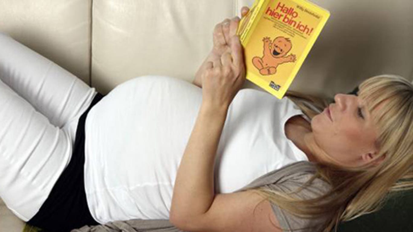 Schwangere im neunten Monat liest Ratgeber auf der Couch.