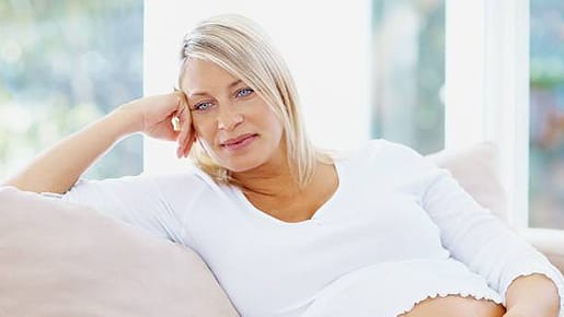 Reife schwangere Frau sitzt nachdenklich auf dem Sofa.