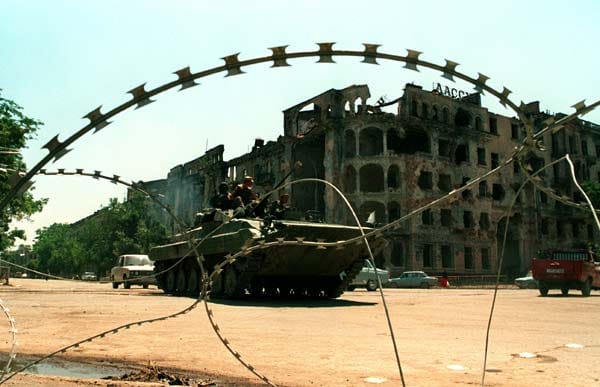 Ein russischer Panzer rollt zwischen Stacheldraht und zerstörten Gebäuden durch die Straßen von Grosny. Im August 1999 greifen russische Truppen erneut an.