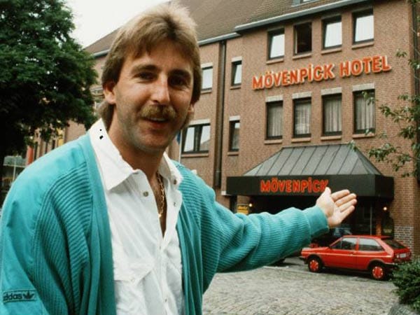 Mit mintgrünem Cardigan zeigt Uwe Reinders, wo er in seiner Anfangszeit als Braunschweiger Trainer wohnt.