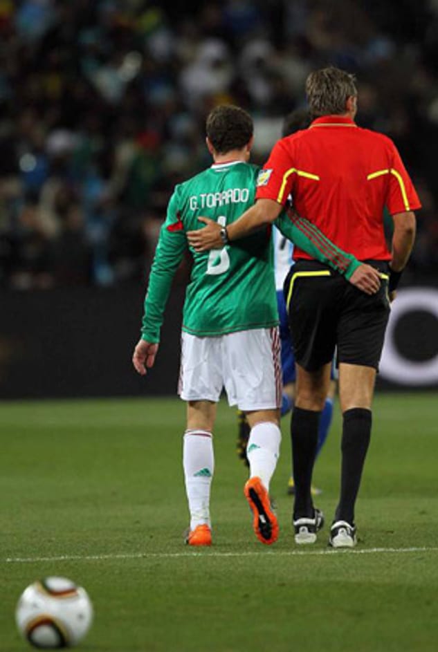 Roberto Rosetti und Mexikos Nationalspieler Gerardo Torrado schlendern engumschlungen über den Platz.