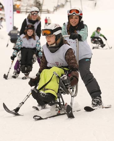 Schüler aus Garmisch-Partenkirchen unterstützen sich gegenseitig beim Erlernen des Monoskifahrens. Die Schüler bekommen so einen Einblick in die Lebenswelt behinderter Menschen. Das Ziel des Projekttages ist erreich.