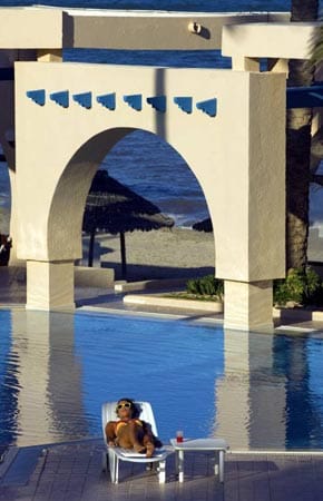 Eine junge Frau nimmt am Pool eines luxuriösen Hotels in Tunesien ein Sonnenbad.