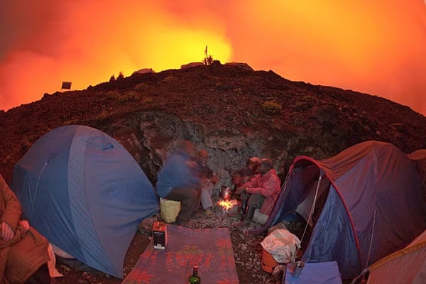 Camping extrem: Nachts erleuchtet der Lavasee den Himmel, flammenrote Wolken stehen über dem Berggipfel im Widerschein des Kratersees.