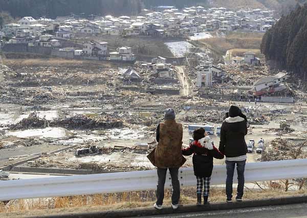 Zwei Erwachsene und ein Kind schauen am 18. März 2011 auf die Stadt Minami Sanriku in der Präfektur Miyagi. Wo eine Woche zuvor noch Häuser standen, erstreckt sich jetzt ein ausgedehntes Trümmerfeld. (Foto: Kyodo / dpa)