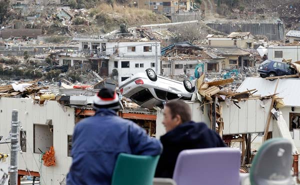 Zwei Einheimische unterhalten sich auf mitgebrachten Stühlen vor der Kulisse der vom Tsunami schwer getroffenen Stadt Onagawa.
