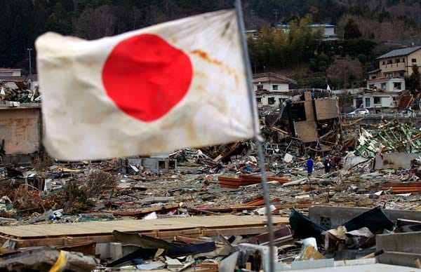 Eine japanische Nationalflagge weht vor dem Hintergrund der Verwüsteten Stadt Onagawa.