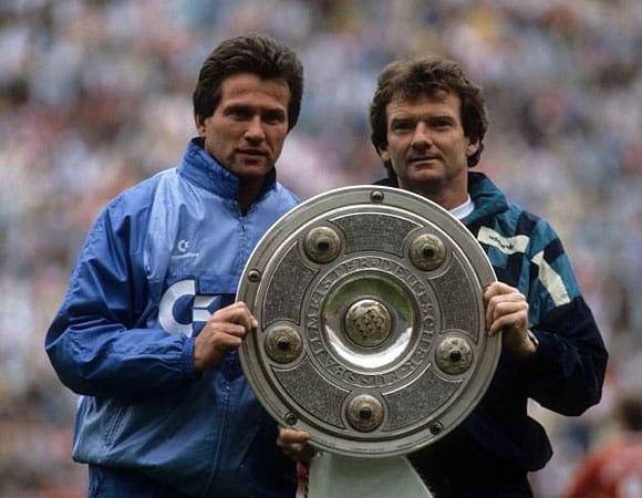 1987 verpflichtet ihn der FC Bayern München. Dort baut Heynckes die Mannschaft nach anfänglichen Schwierigkeiten kräftig um. Und der Erfolg gibt ihm Recht. Mit den Bayern holt er 1989 die Meisterschale. Ein Jahr später verteidigt er den Titel. Hier ist er im Bild mit dem damaligen Co-Trainer Egon Cordes (rechts).