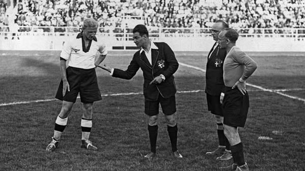 7. Juni 1934 in Neapel: Ganze 9.000 Zuschauer wollen das kleine Finale der zweiten WM verfolgen - und sehen zunächst den Münzwurf des italienischen Schiedsrichters Albino Carraro. Links von ihm der deutsche Kapitän Fritz Szepan, ganz rechts Österreichs Spielführer Johann Urbanek. Urbanek vertritt den verletzten Superstar Matthias Sindelar. Dessen Fehlen mündet in ein 2:3, die erste österreichische Niederlage gegen Deutschland nach zehn Jahren.