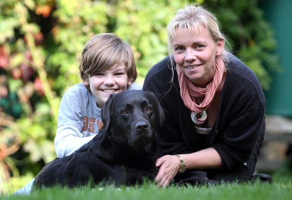 Dieses Foto zeigt den neunjaehrigen Arnold, seine Mutter Berit Quass und Labradorhündin "Lulu" im Gras.