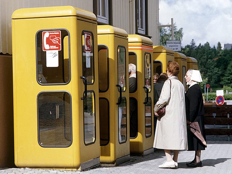 Sechs gelbe Telefonzellen der Deutschen Bundespost mit davor wartenden Kunden, aufgenommen 1985.