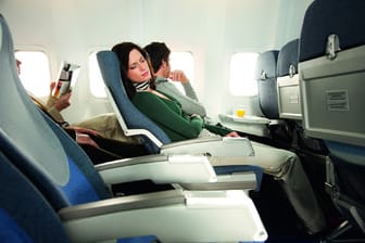 Eine Frau schläft im Flugzeug: Wer viel reist, sollte über eine Langzeit-Auslandskrankenversicherung nachdenken.