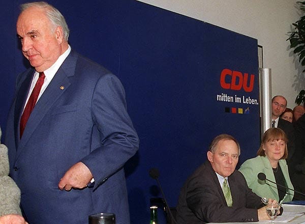 Kohl verlässt im November 1999 frühzeitig eine Pressekonferenz zur CDU-Spendenaffäre mit dem damaligen CDU-Vorsitzenden Wolfgang Schäuble und Generalsekretärin Angela Merkel. In der Affäre um schwarze Konten und anonyme Geldspenden in Millionenhöhe bricht Merkel mit ihrem langjährigen Förderer. Sie zwingt ihn, vom Amt des CDU-Ehrenvorsitzenden zurückzutreten.