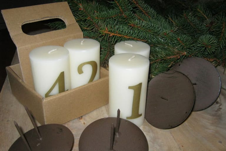 Kerzenhalter und Adventskerzen: Nachdem Sie die Zweige wie gewünscht drapiert haben, sind die Kerzen an der Reihe. Für einen Adventskranz greift man meist zu dickeren Kerzen, aber auch dünne Kerzen können schön aussehen. Auf Adventskränzen machen sich auch nummerierte Kerzen gut.