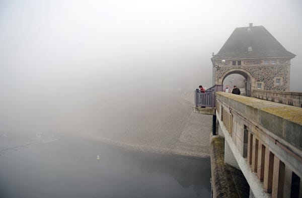 Touristen stehen auf der Staumauer des nordhessischen Edersees. Nicht nur wegen des Nebels sehen sie kaum das Wasser.