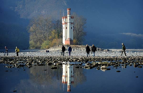 Spaziergänger gehen in Bingen am Rhein über die wegen des Niedrigwassers freiliegenden Kiesbänke zum Binger Mäuseturm.