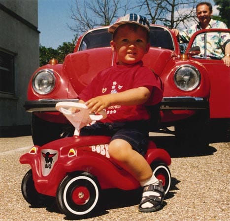 Für die meisten Kinder die erste Erfahrung am Lenkrad: ein Bobby-Car aus den 70er Jahren vor einem VW Käfer.