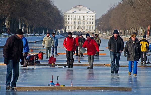 Männer spielen auf dem zugefrorenen Nymphenburger Kanal in München Eisstockschießen.