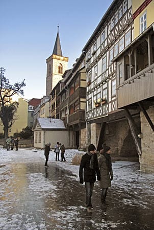 Passanten gehen auf einem zugefrorenen Nebenarm des Flusses Gera in Erfurt an der historischen Krämerbrücke vorbei.