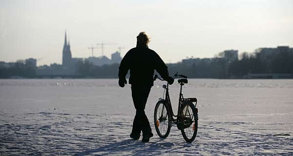Ein Mann schiebt in Hamburg ein Fahrrad über die zugefrorene Außenalster.