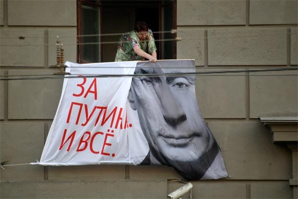 Eine Frau holt in Moskau ein Putin-Werbeplakat ein.
