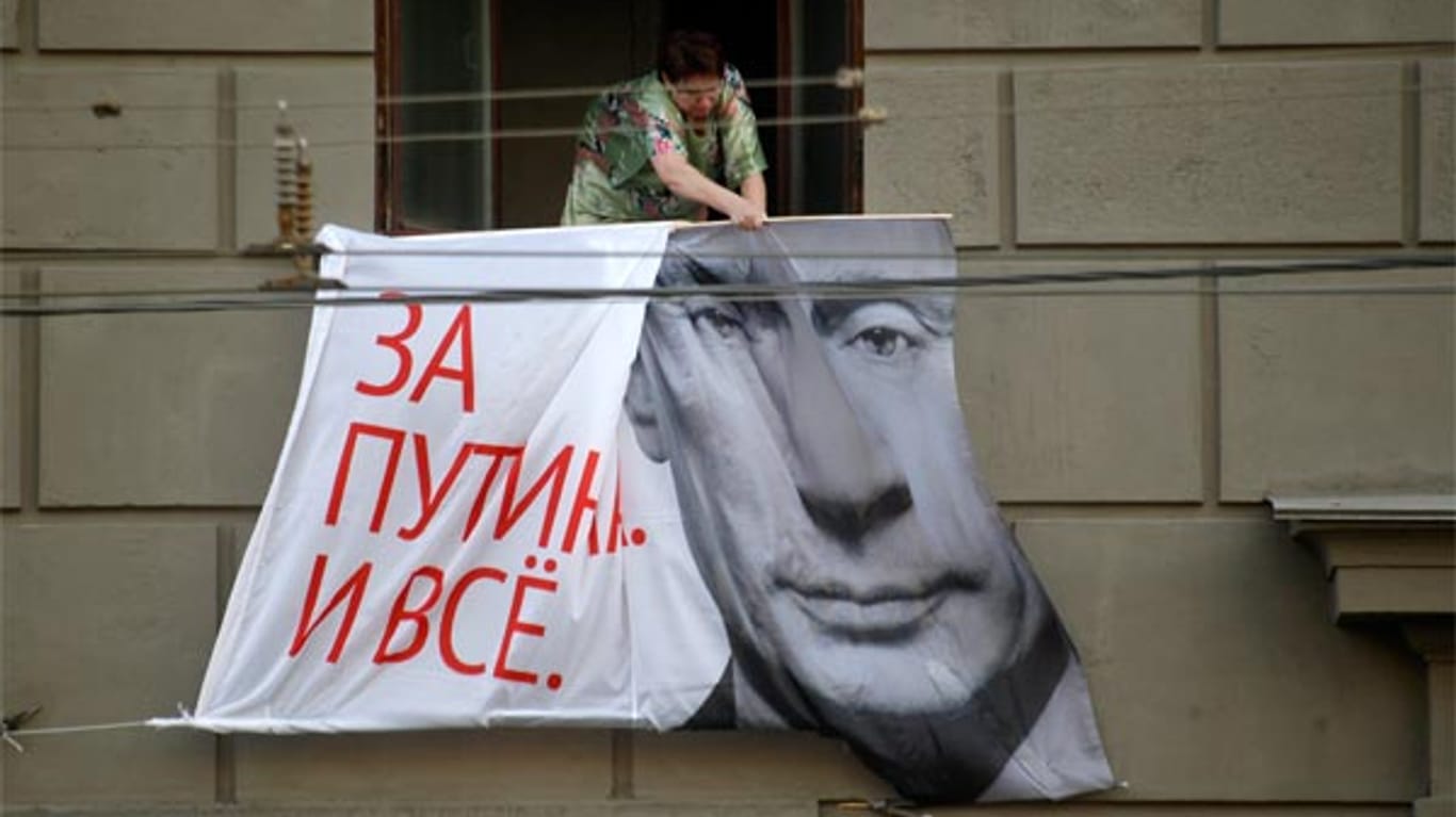Eine Frau holt in Moskau ein Putin-Werbeplakat ein.