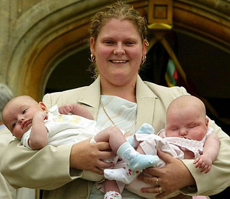 Louise Brown, die als weltweit erstes Retortenbaby berühmt wurde, hält am 26.07.2003, ihrem 25. Geburtstag, die Babys Henry (l) und Antonia Veary im Arm. Sie steht vor der Klinik in Bourn Hall, die von den Ärzten gegründet wurde, die ihr einst das Leben schenkten.