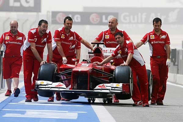 Ferrari-Mechaniker schieben den Boliden von Fernando Alonso durch die Boxengasse.
