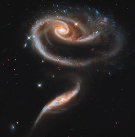 Äußerst fotogen präsentiert sich diese spiralförmige Gruppe interagierender Galaxien. Die blau-glitzernden Punkte oben sind Cluster von intensiv strahlenden, heißen Jungsternen.